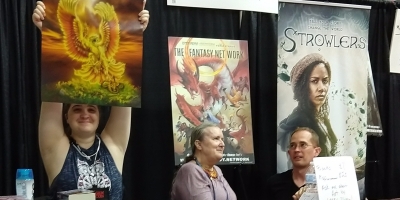 Mercedes Lackey (center) at the Zombie Orpheus Entertainment stall. The person at left holds up a print of one of Larry Dixon's paintings.